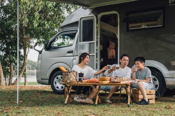 Happy Asian family talking at picnic table by the camper trailer in nature Happy Asian parents and their kid communicating while spending a spring day on camping. - Camper van travel series family fun outing stock pictures, royalty-free photos & images